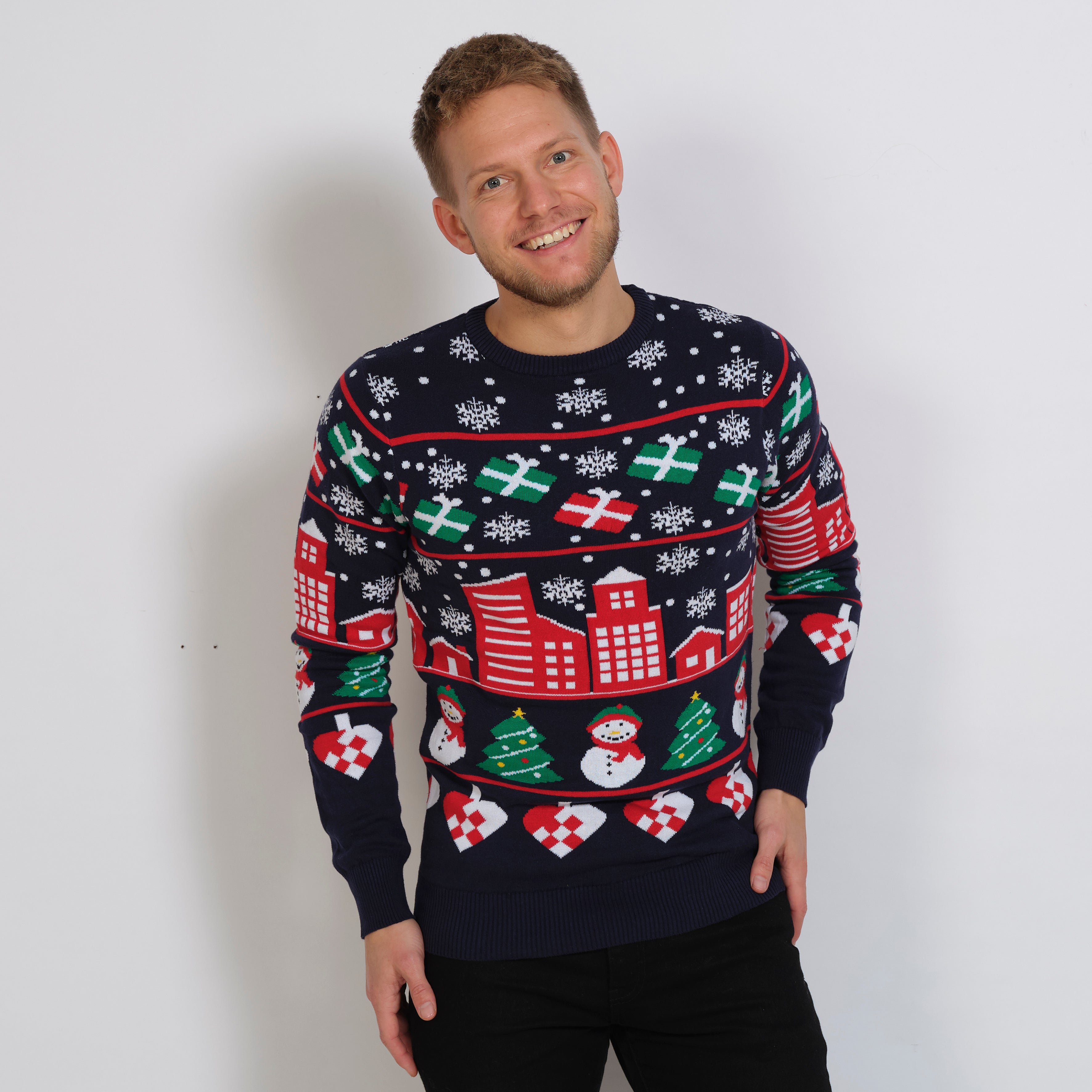 En mand med en blå julesweater på, hvor der er råde huse, gaver og snefnug.